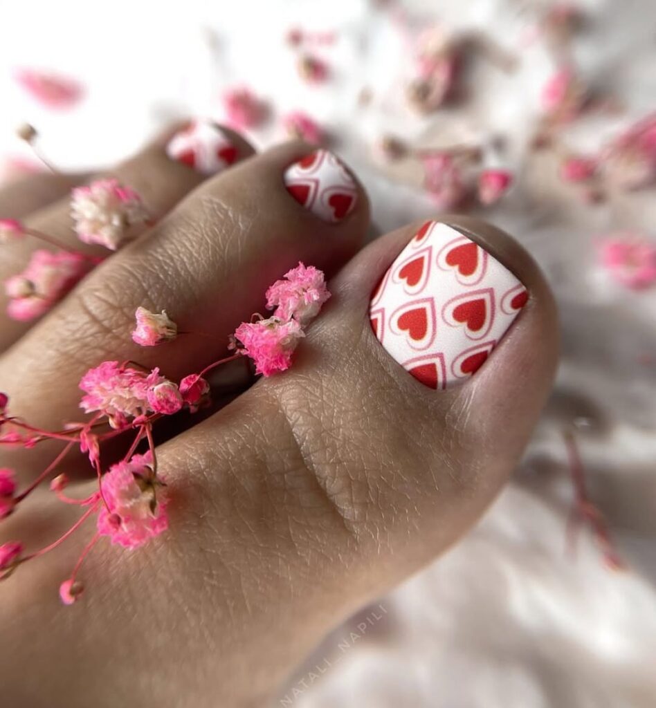 Pedicure z czerwonymi sercami na białym tle w otoczeniu różowych kwiatów