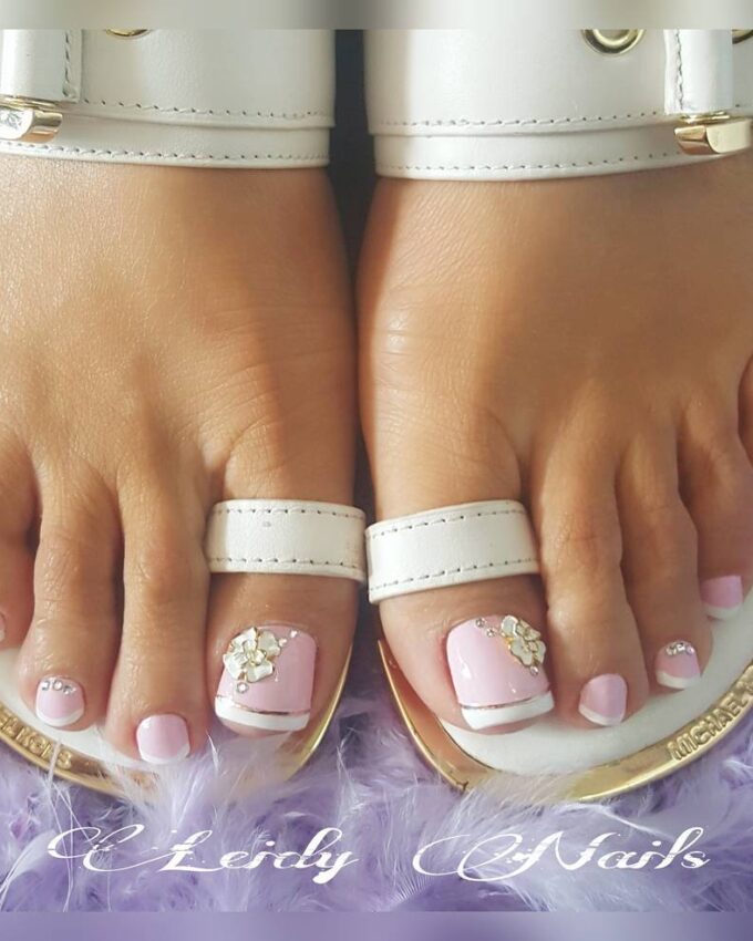 Delikatny różowy pedicure z białymi liniami i ozdobnymi cyrkoniami w kształcie kwiatka
