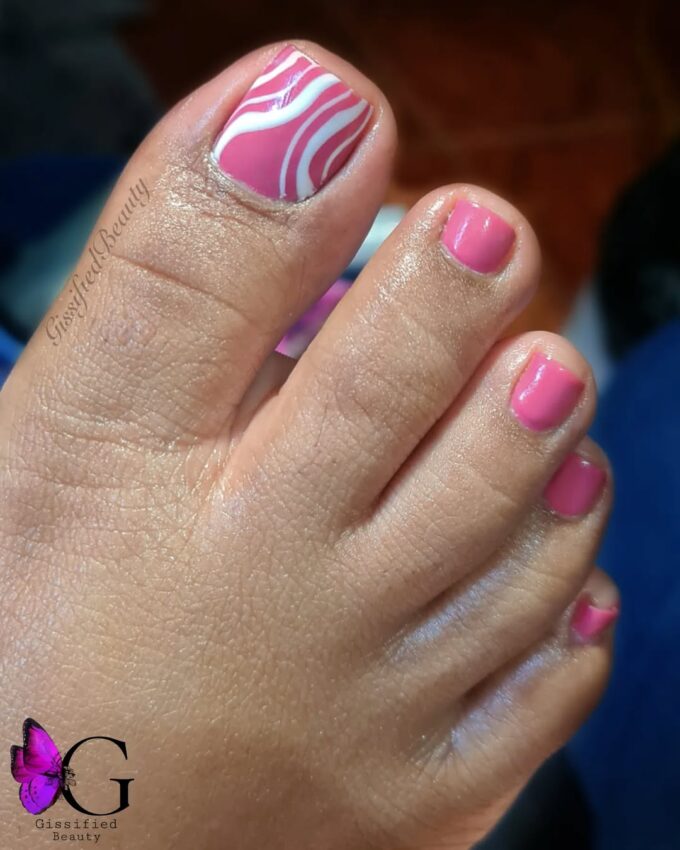 Różowy pedicure z białymi, falowanymi wzorami na dużym paznokciu