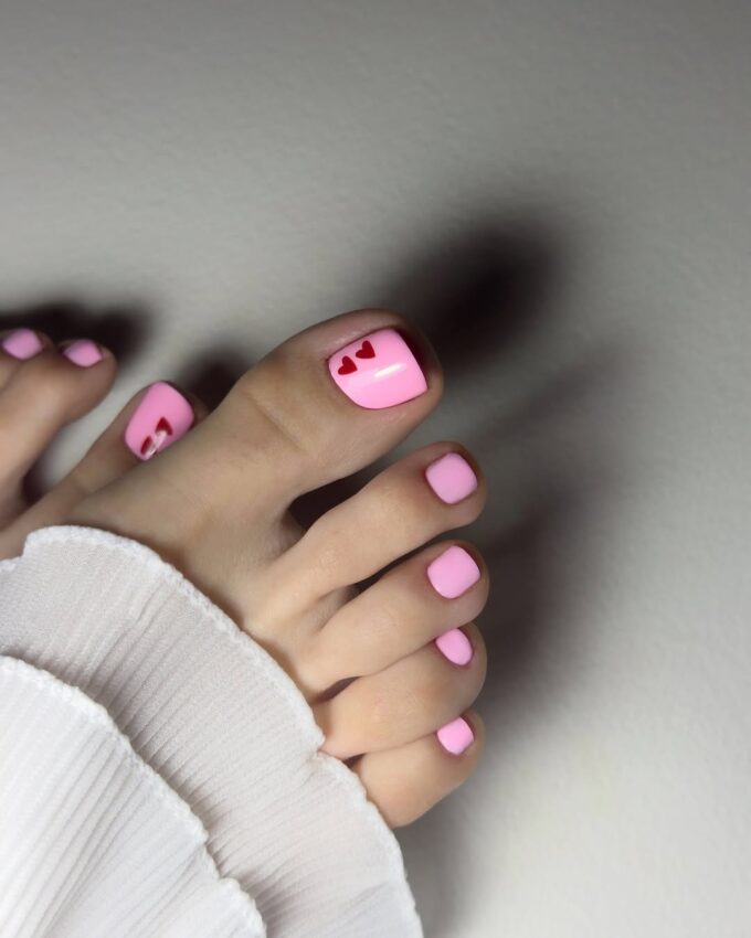 Jasnoróżowy pedicure z czerwonymi serduszkami na dużym paznokciu
