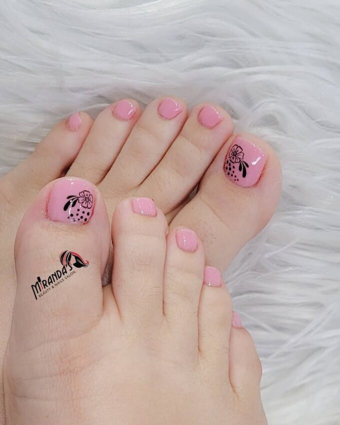 Jasnoróżowy pedicure z delikatnym czarnym wzorem kwiatowym na dużych paznokciach